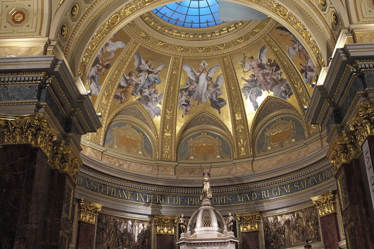 The sanctuary vault of St Stephen's Basilica with painted figures, gilded ornament and a skylight, above a band of lettering.