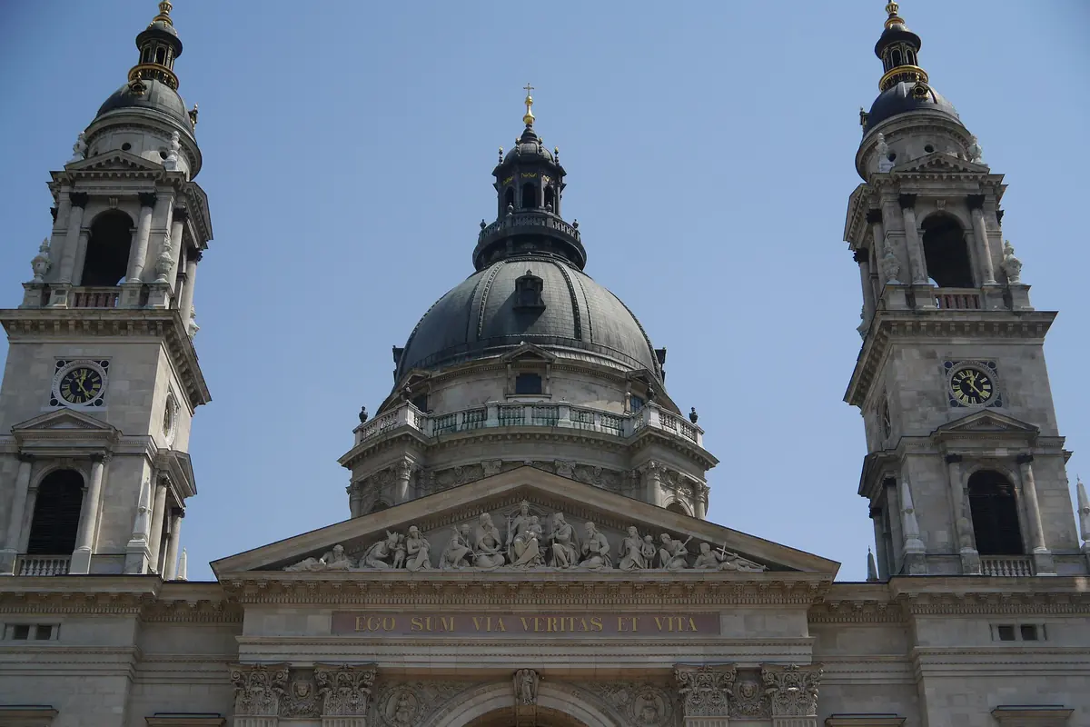 The towers, dome and pediment of the basilica seen from below against a blue sky.