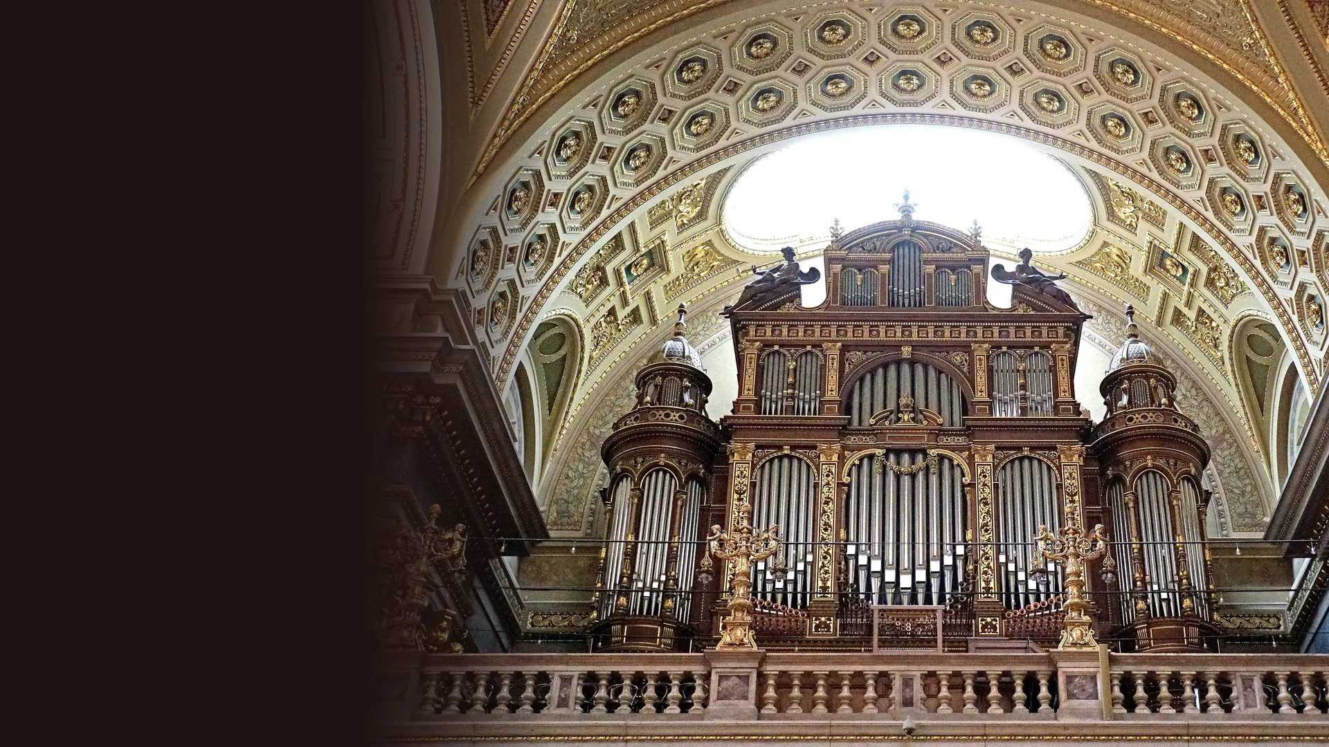 The organ of St Stephen's Basilica in Budapest: a dark wood case with gilded ornament and silver pipes under a coffered arch with a pale skylight behind it.